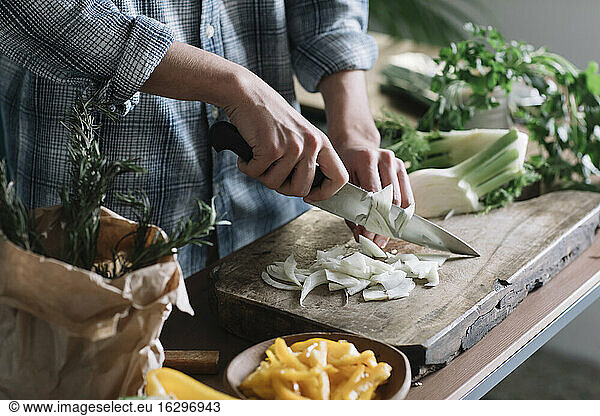 Midsection of young man cutting fennel on board in kitchen