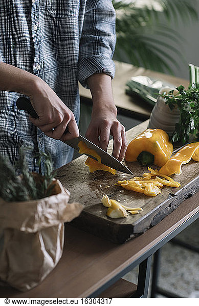 Midsection of young man cutting yellow bell pepper on board in kitchen