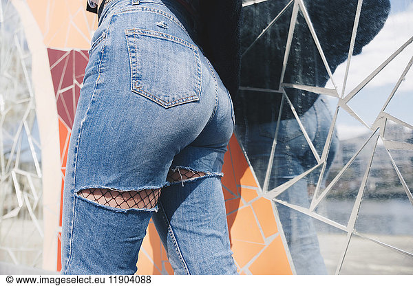 Midsection of young woman wearing torn jeans against mosaic wallMidsection of young woman wearing torn jeans against mos