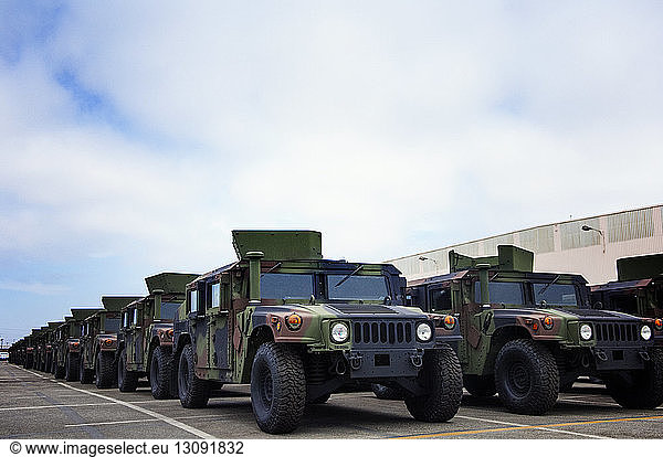 Military vehicles parked at industry against cloudy sky