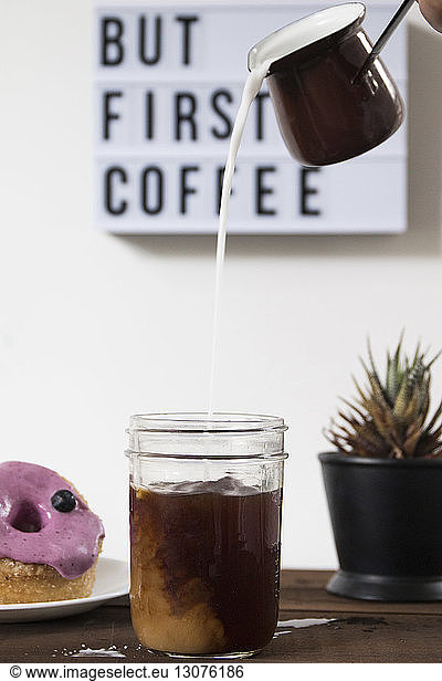 Milk pouring in coffee by donut on wooden table