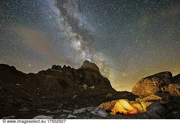 Milky Way galaxy stretching against night sky over lone illuminated tent in Maira Valley