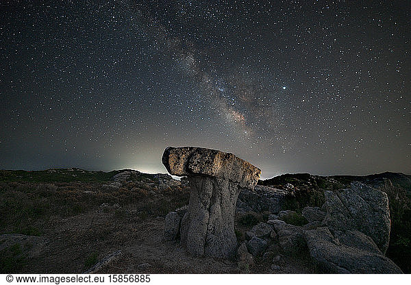milky way panorama above a mushroom-shaped rock