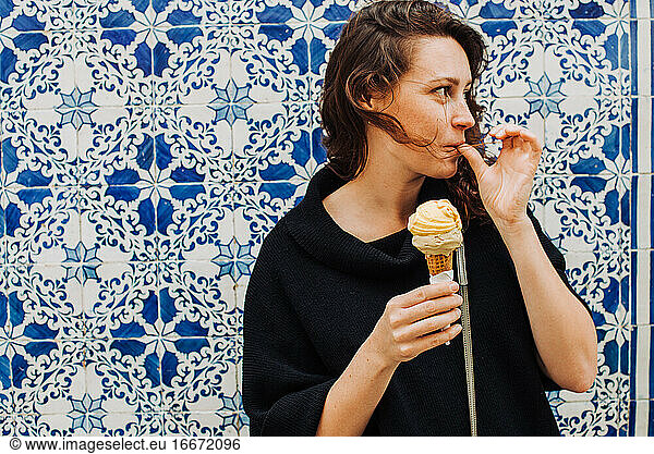 Millennial Frau leckt Finger beim Essen Eis an einer gekachelten Wand
