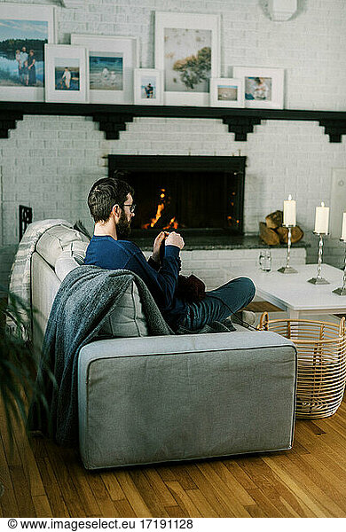 Millennial man crocheting in his living room by the warm and cozy fire