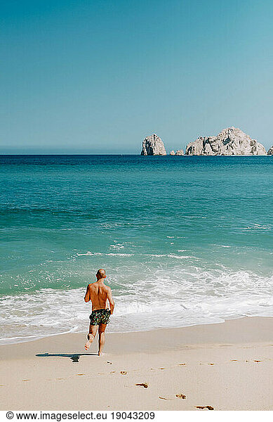 Millennial man runs on Cabo San Lucas beach.