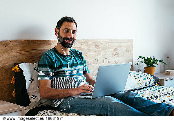Millennial-Mann arbeitet zu Hause im Bett am Laptop