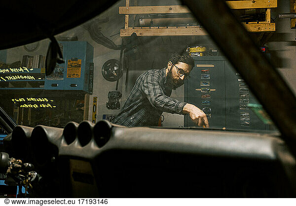 Millennial-Mann in der Garage  der den Motor eines alten Autos repariert