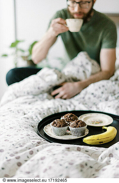 Millennial-Mann trinkt Frühstückstee im Bett  während er sein Smartphone bedient
