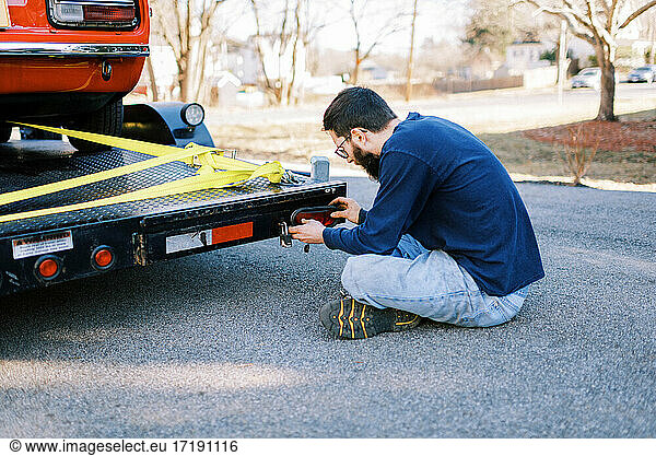 Millennial-Mechaniker in der Einfahrt bei der Reparatur des Rücklichts eines Autotransporters
