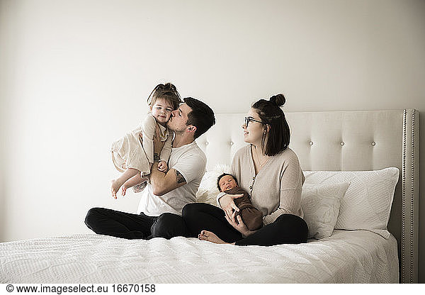 Millennial-Vater küsst seine kleine Tochter  während er mit der Familie zusammensitzt