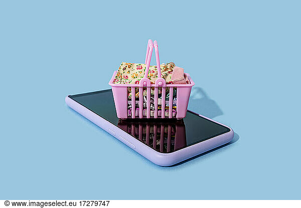 Miniature shopping basket lying on top of smart phone
