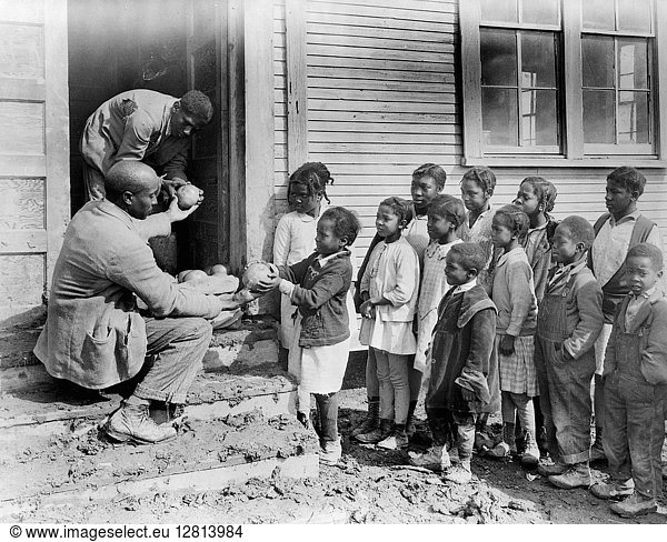 MISSISSIPPI: FOOD RELIEF. School teacher providing fruit from the Red Cross to African American children  Shaw  Mississippi. Photograph by Lewis Wickes Hine  c1931.