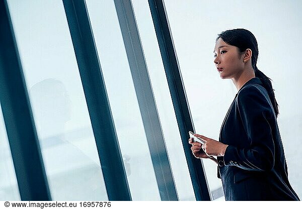 Mit einem Mobiltelefon steht eine Geschäftsfrau vor dem Fenster