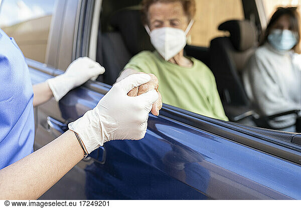 Mitarbeiterin im Gesundheitswesen hält die Hand eines älteren Patienten  der im Auto sitzt