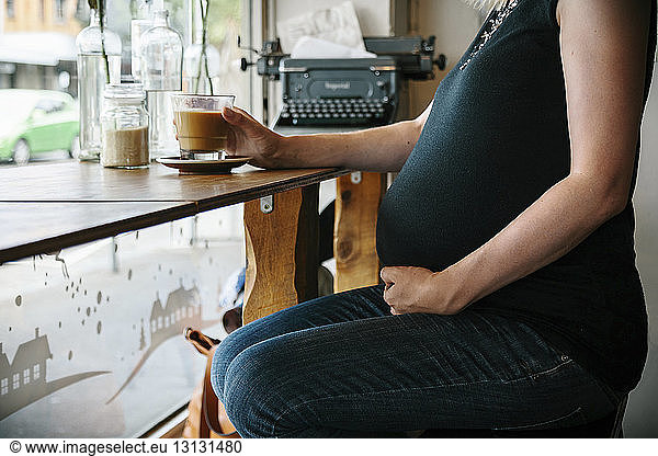 Mitschnitt einer schwangeren Frau  die Kaffee trinkt  während sie im Café am Fenster sitzt
