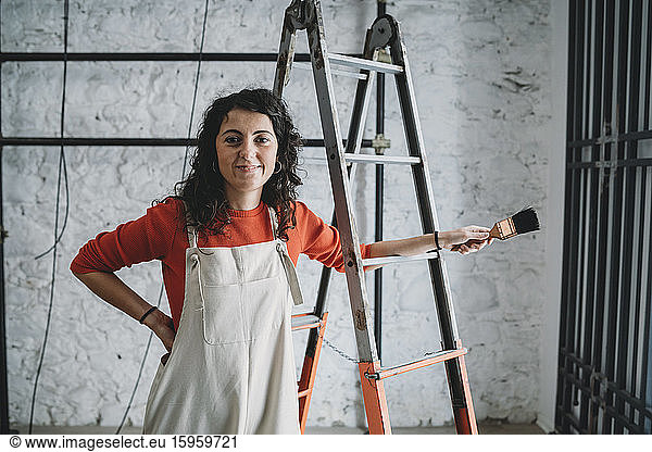 Mittelgroße erwachsene Frau  die in ihrem neuen Geschäft mit Pinsel auf einer Trittleiter lehnt  Porträt
