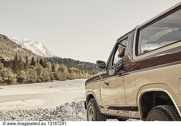 Mittelgroßer erwachsener Mann im Pickup  lehnt aus dem Fenster und schaut auf ein Gebirge  Wallgau  Bayern  Deutschland