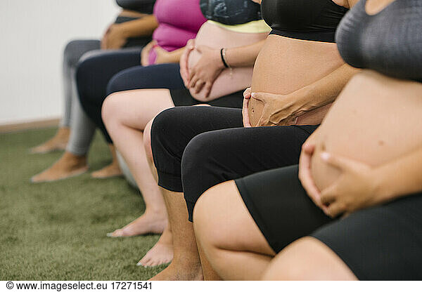 Mittelteil einer schwangeren Frau  die im Yogastudio mit den Händen auf dem Bauch sitzt
