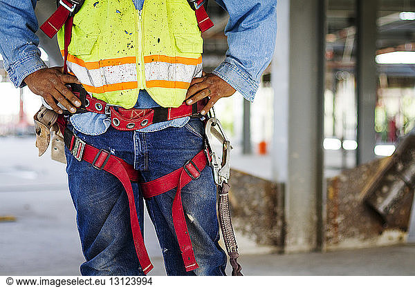 Mittelteil eines auf der Baustelle stehenden Arbeiters mit Sicherheitsgurt