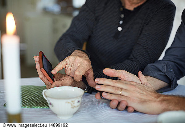 Mittelteil eines reifen Mannes  der auf ein Smartphone zeigt und auf einen Freund auf dem Tisch zeigt