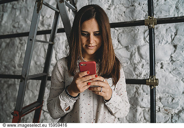 Mittlere erwachsene Frau betrachtet Smartphone in ihrem neuen Geschäft