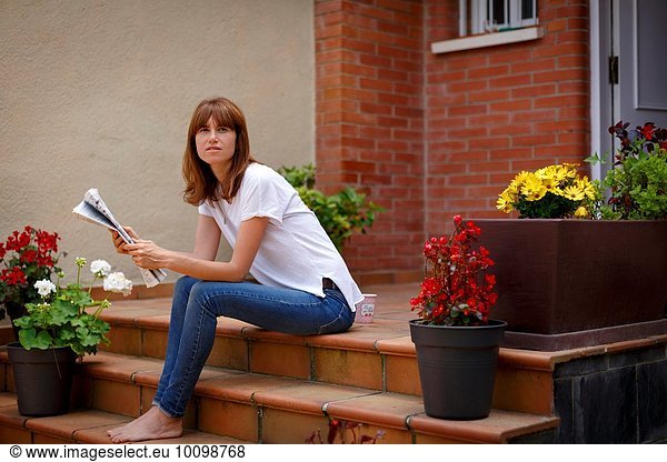 Mittlere erwachsene Frau im Freien sitzend  Zeitung haltend  Kamera betrachtend