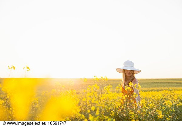 Mittlere erwachsene Frau im Rapsfeld mit Sonnenhut  Blick nach unten  Fokus auf den Hintergrund