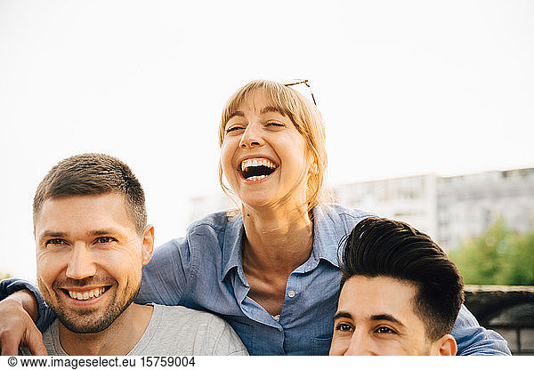 Mittlere erwachsene Frau lacht  während sie bei einem geselligen Beisammensein bei männlichen Freunden steht