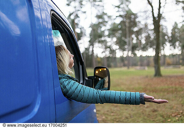 Mittlere erwachsene Frau lehnt ihre Hand aus dem Fenster eines Wohnmobils an einem regnerischen Tag