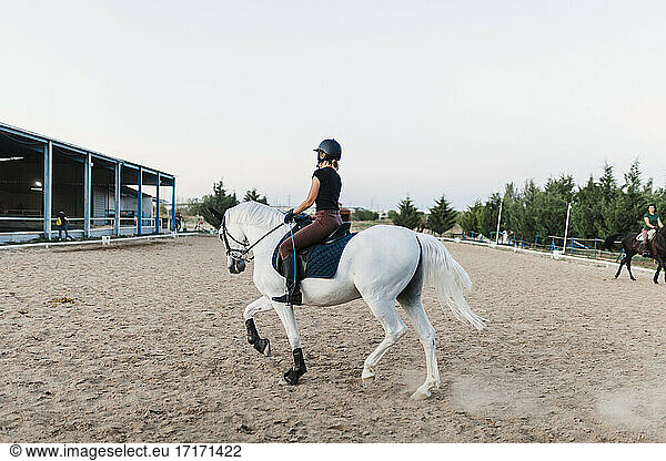 Mittlere erwachsene Frau mit Kopfbedeckung reitet am Wochenende auf einem Reiterhof