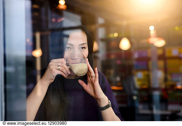 Mittlere erwachsene Frau trinkt Kaffee am Fensterplatz eines Cafés