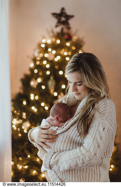 Mittlere erwachsene Frau wiegt neugeborene Tochter zu Weihnachten in Strickjacke gewickelt