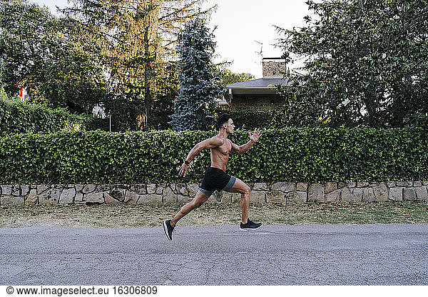 Mittlerer erwachsener männlicher Athlet  der auf der Straße gegen Pflanzen im Hof läuft