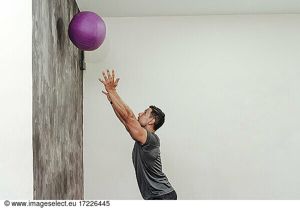 Mittlerer Erwachsener  männlicher Athlet  der mit einem Medizinball an einer Wand im Fitnessstudio trainiert