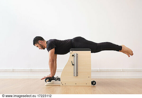 Mittlerer erwachsener Mann  der auf einem Stuhl liegt  während er im Übungsraum Pilates praktiziert
