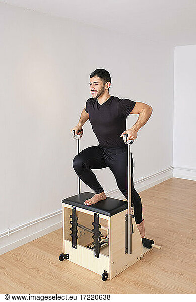 Mittlerer erwachsener Mann  der sich beim Pilates auf einem Stuhl im Übungsraum dehnt