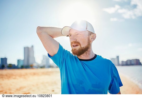 Mittlerer erwachsener Mann mit Baseballmütze  Hand hinter dem Kopf wegblickend  Dubai  Vereinigte Arabische Emirate