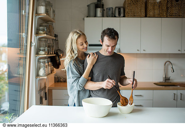Mittleres erwachsenes Paar beim Mischen von Salatschüsseln in der Küche