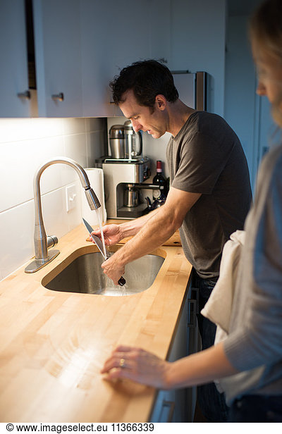 Mittleres erwachsenes Paar beim Waschen des Küchenmessers am Spülbecken