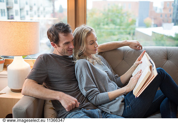 Mittleres erwachsenes Paar  das auf dem Sofa liegt und ein Buch liest.