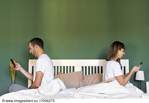 Mittleres erwachsenes Paar  das ein Mobiltelefon benutzt  während es zu Hause auf dem Bett sitzt