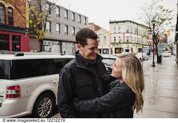 Mittleres erwachsenes Paar  das sich auf der Straße umarmt und lächelt