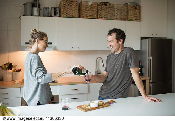 Mittleres erwachsenes Paar gießt Rotwein in die Küche