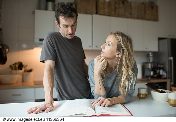 Mittleres erwachsenes Paar liest Rezeptbuch in der Küche