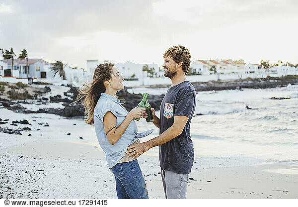 Mittleres erwachsenes Paar stößt auf Getränke an  während sie am Strand stehen