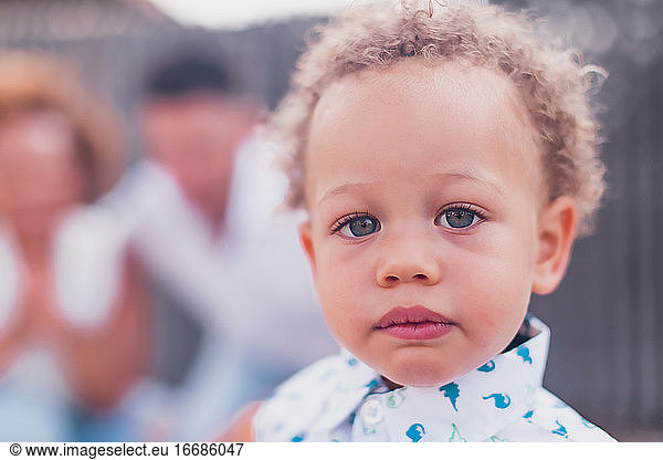 Mixed race boy with blue eyes looking at camera and parents on back