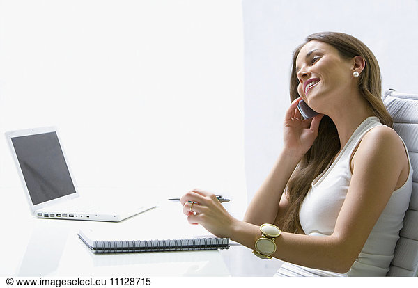 Mixed race businesswoman talking on cell phone at desk