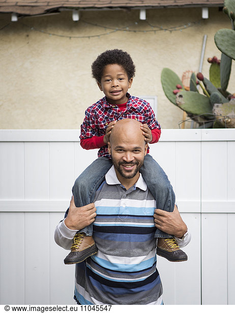 Mixed race father carrying son on shoulders