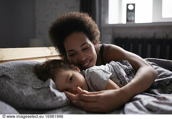 Mixed race mother hugging daughter in morning